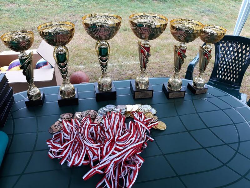 Puchary sportowe ustawione w rzędzie wraz z medalami na stole podczas mityngu lekkoatletycznego.